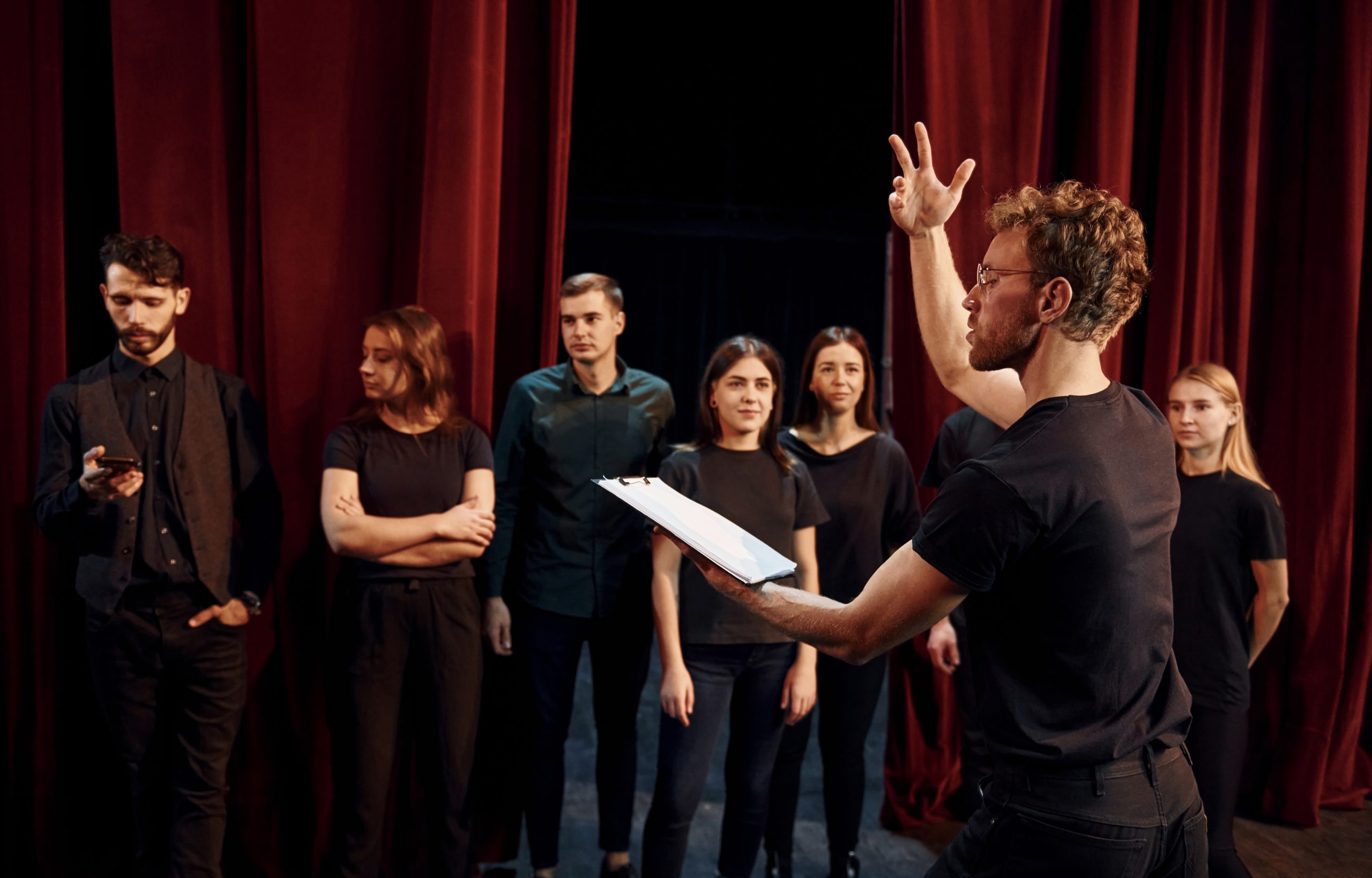 Man with notepad practice his role. Group of actors in dark colored clothes on rehearsal in the theater